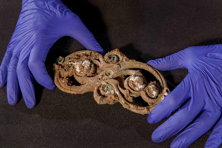 Gloved hands holding a piece of Iron Age metal featuring intricate scrollwork