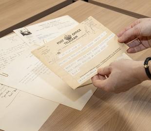 A close up of a person holding a telegram over a pile of archive documents